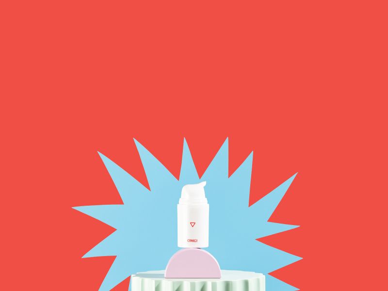 A bottle of OMG! Cream sits on colorful abstract shapes with a blue starburst pattern and a red background