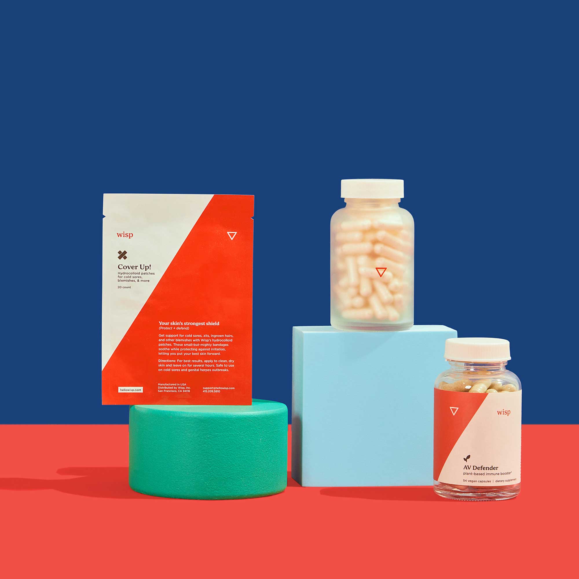Wisp Cover Up! Hydrocolloid patches, a tall glass pill jar, and AV Defender balanced on colorful abstract shapes on a red surface with a blue background