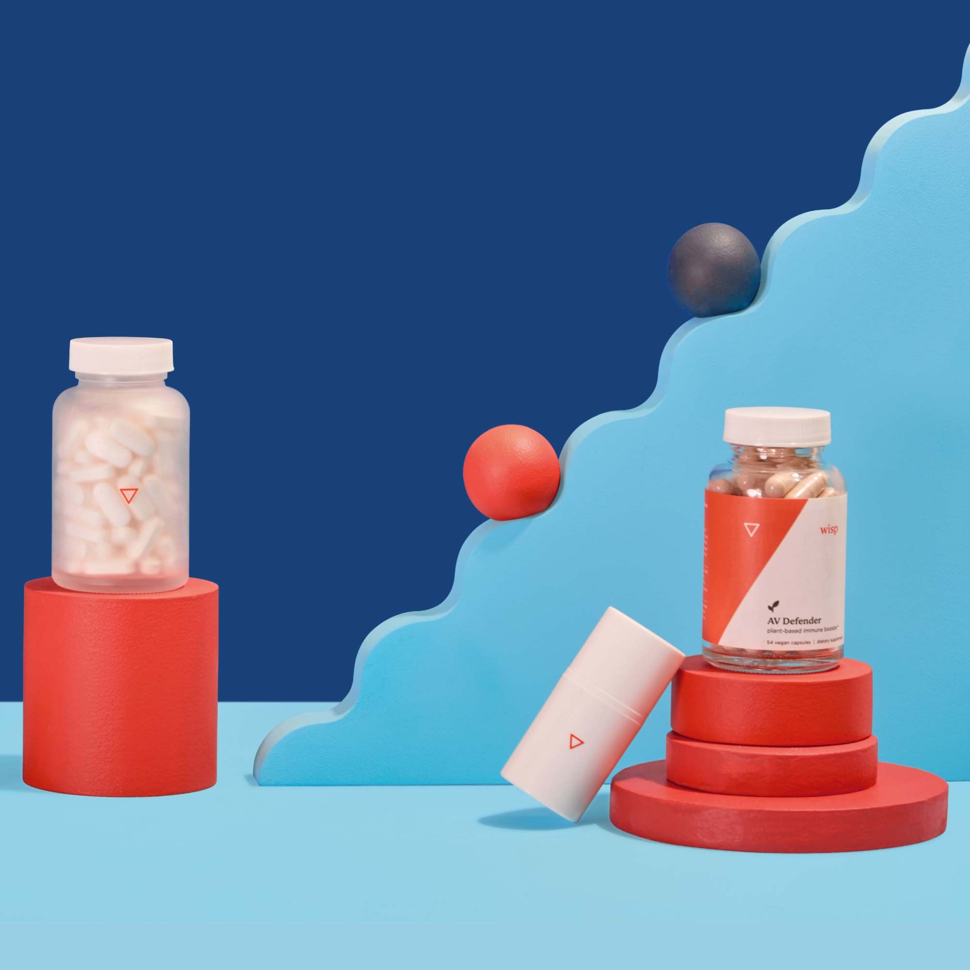 A tall glass pill jar, a plastic pump bottle and a clear supplement bottle are balanced on colorful abstract shapes with a light blue surface and a dark blue background