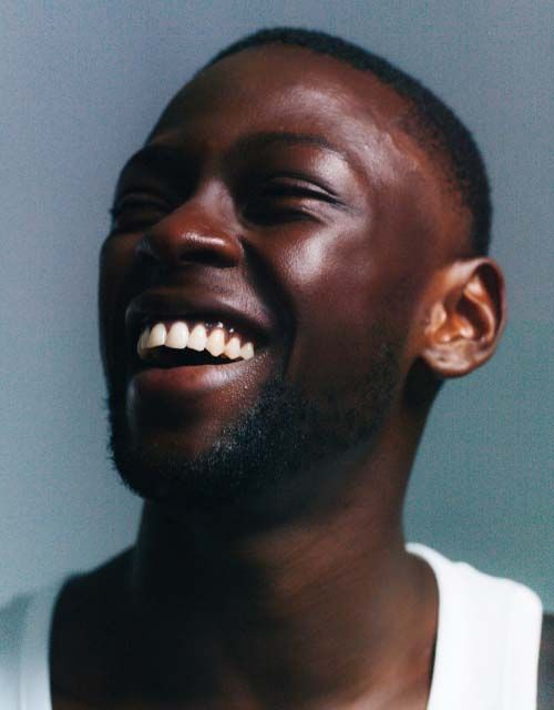 A smiling man wearing a white tank top with a gray background