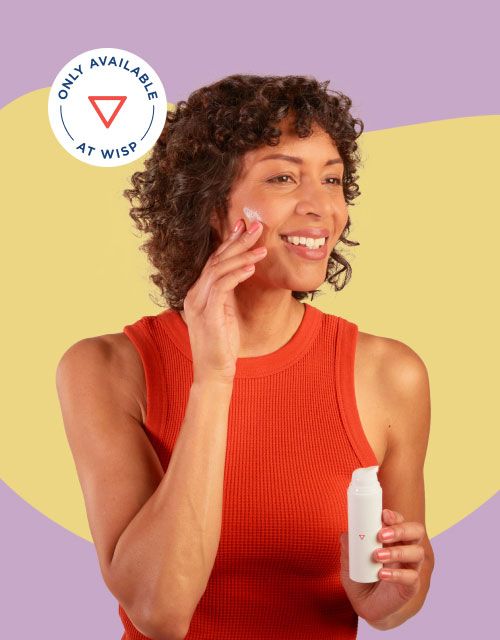 A smiling woman wearing a red tank top is apply Wisp Topical Spironolactone to her face