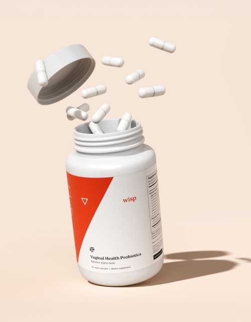 A bottle of Wisp Vaginal Probiotics with pills and the lid floating outside the bottle with a cream background