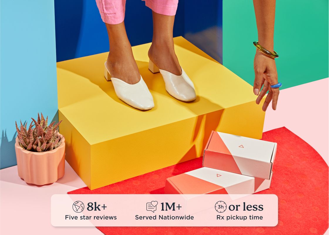 A woman standing on a colorful door step is reaching for Wisp shipping boxes