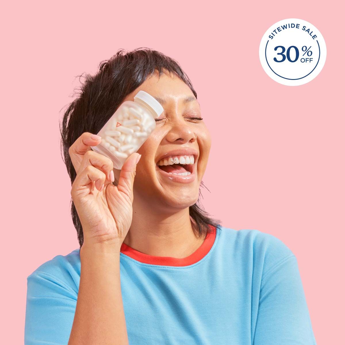 A woman smiling and wearing a blue shirt while holding a Wisp glass pill jar in front of a pink background