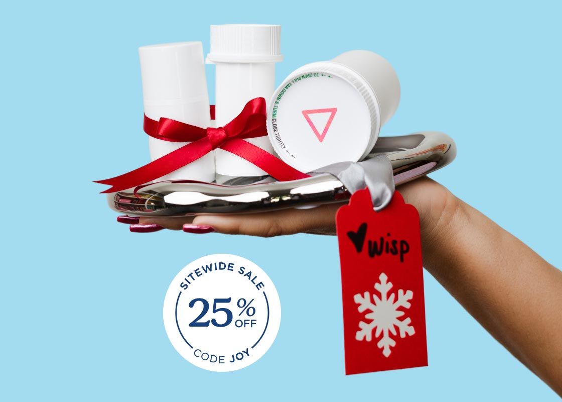 A persons hand holding a silver tray with Wisp medication vials on it with a red ribbon and gift tag in front of a light blue background