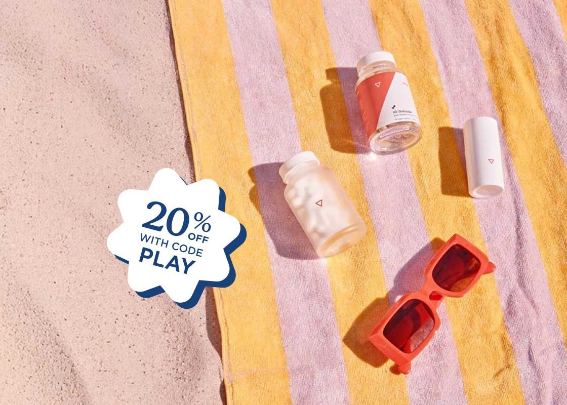 Various Wisp products with red sunglasses on a pink and yellow striped beach towel on sand