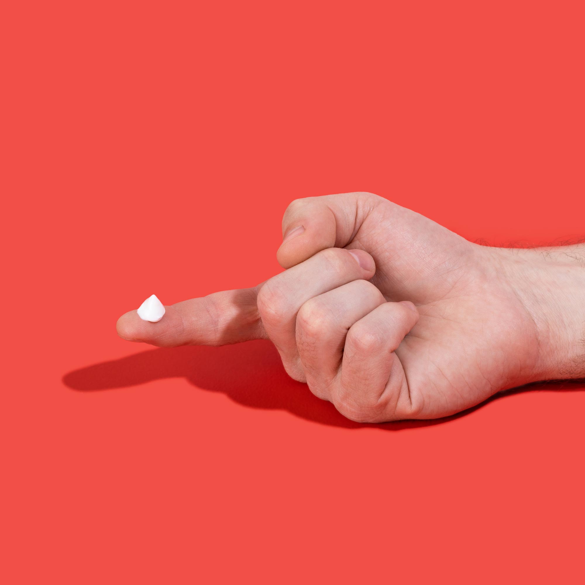 Hand with smear of topical lidocaine cream on finger on red background