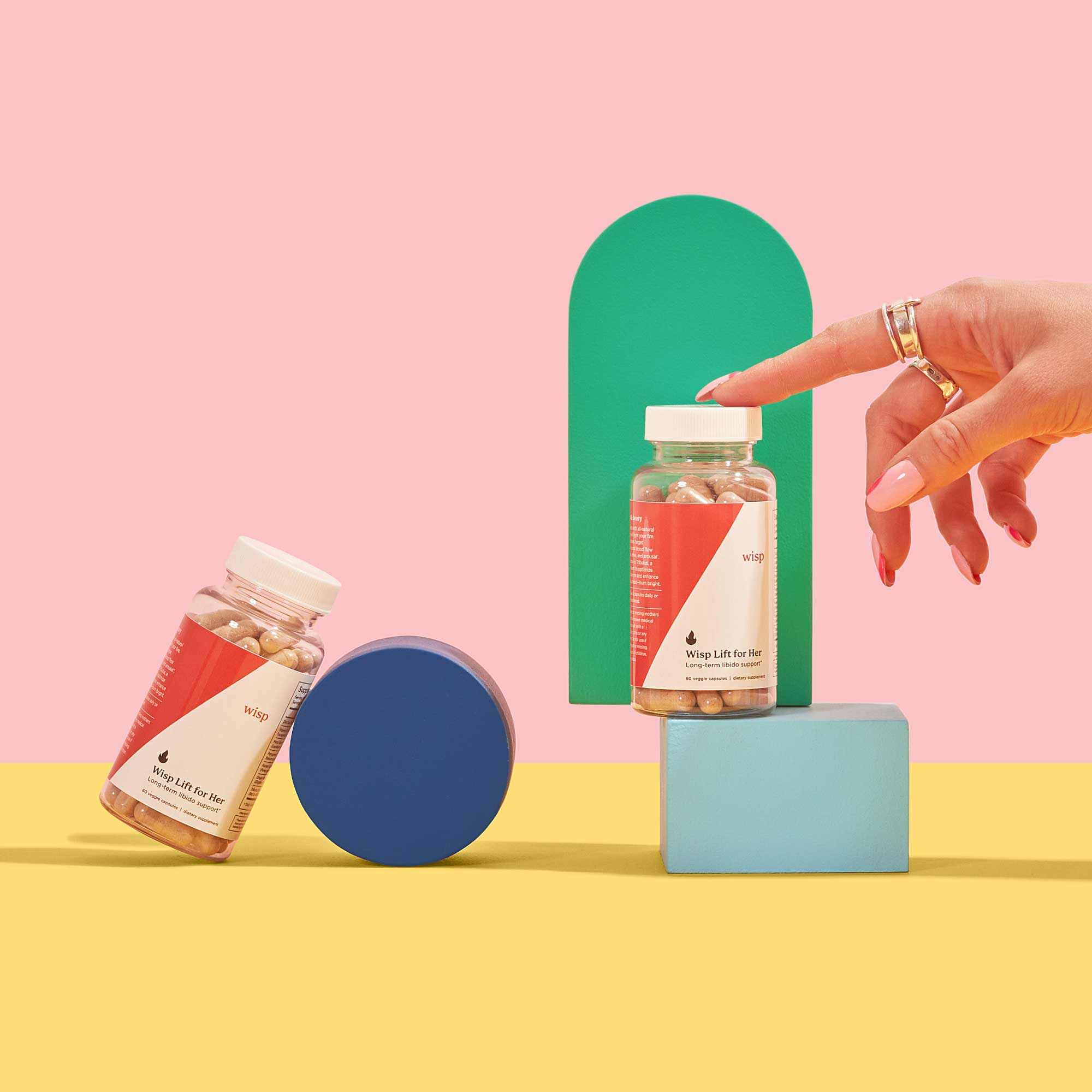 Two bottles of Wisp Lift for her balanced on colorful abstract shapes on a yellow surface with a pink backgound