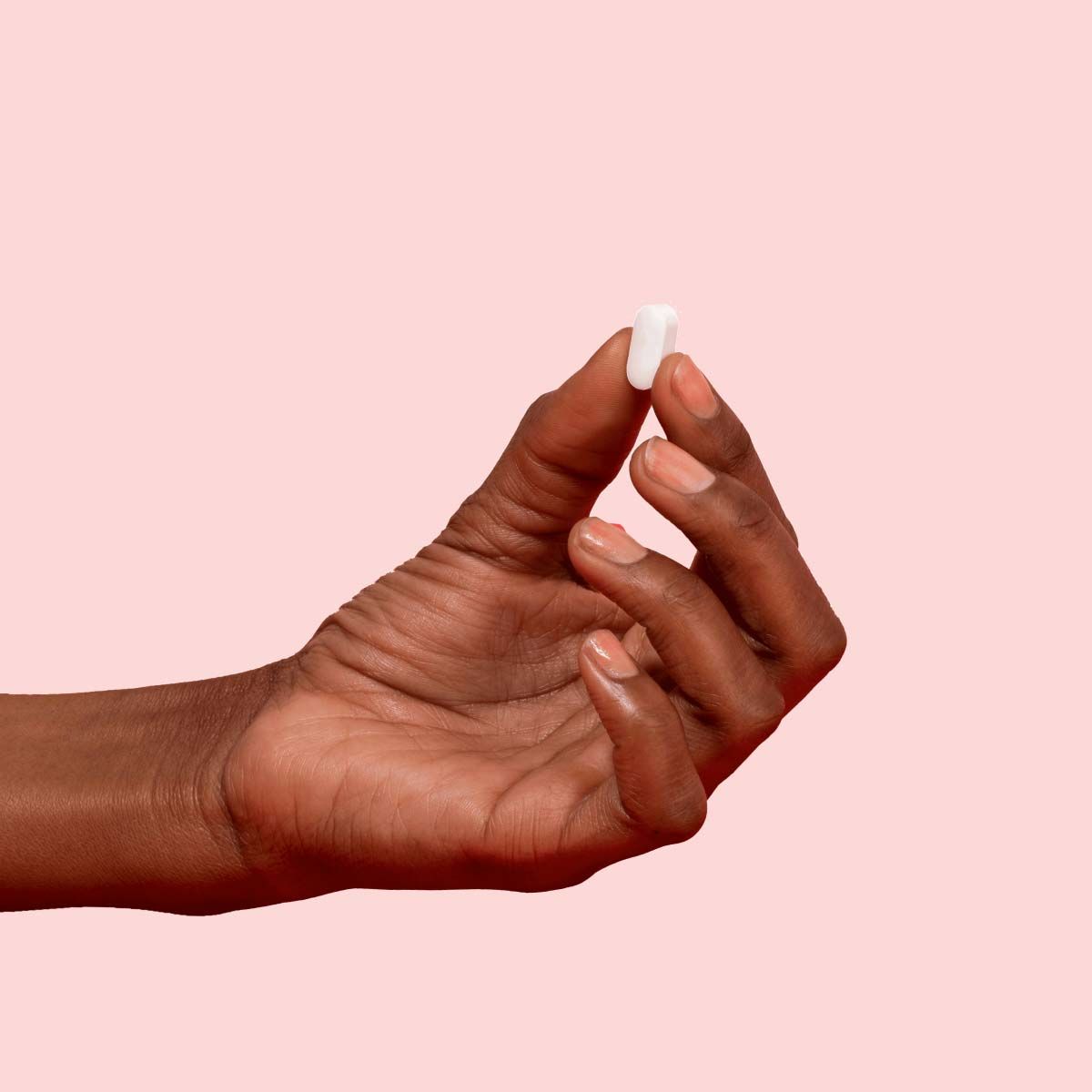 A person's hand holding a Metformin pill between their thumb and index finger with a pink background