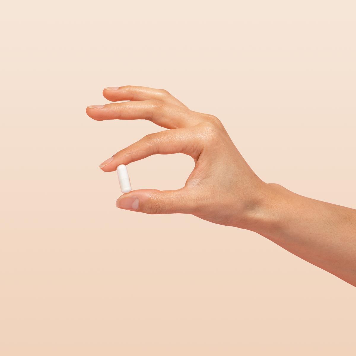 A person's hand holding a white capsule with a cream background