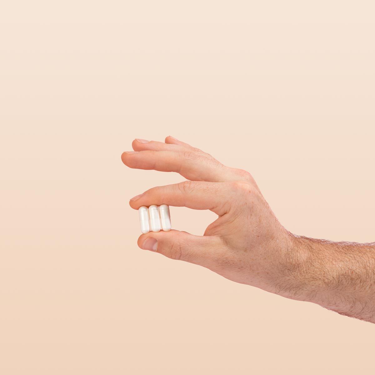 Hand holding lysine capsules with a cream background