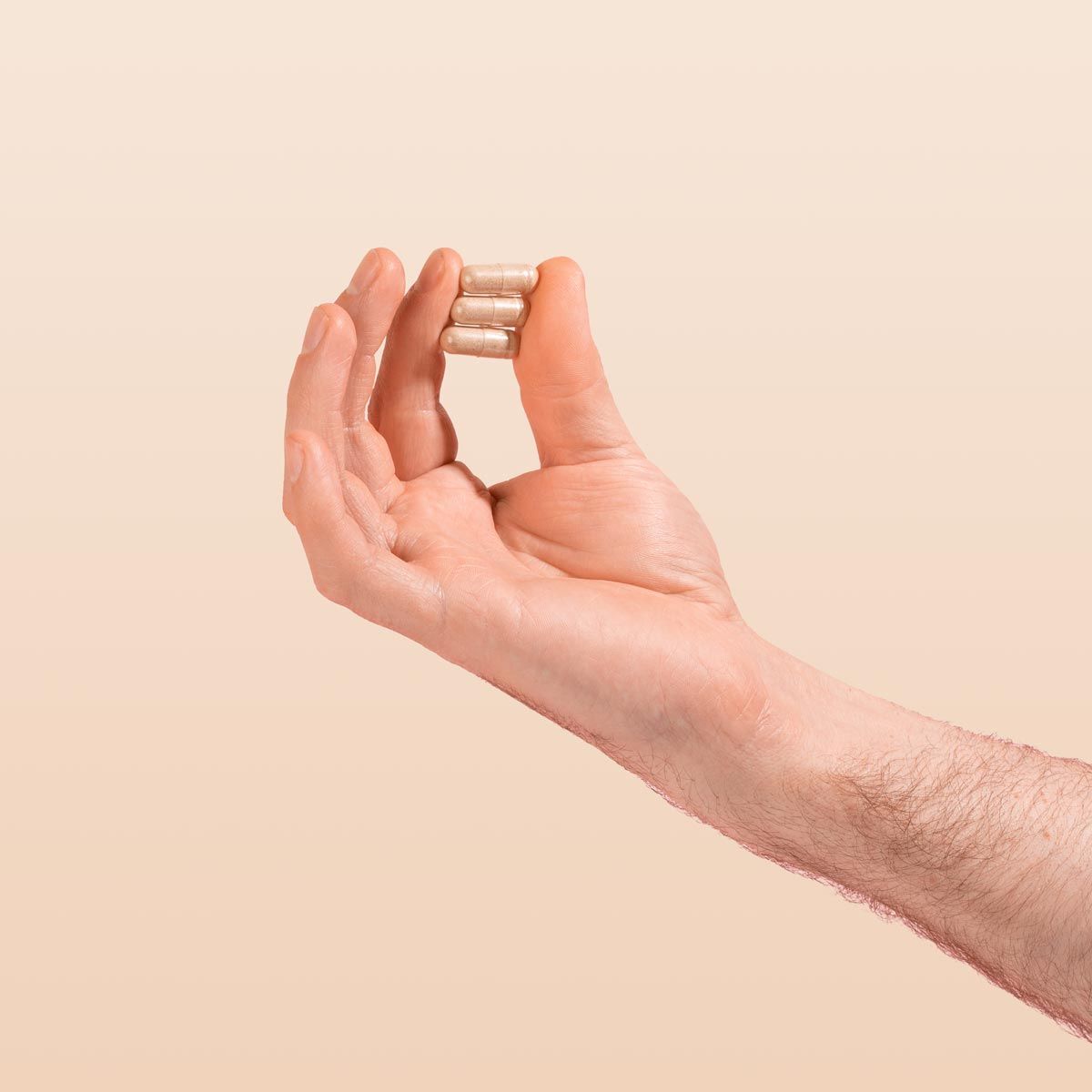 Male hand holding AV Defender capsules on a cream background