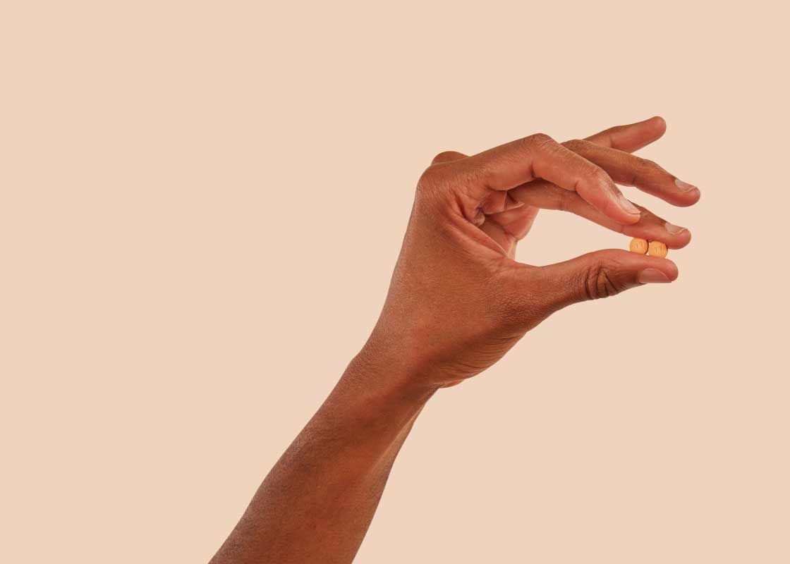 A man's hand holding a DoxyPEP pill with a beige background