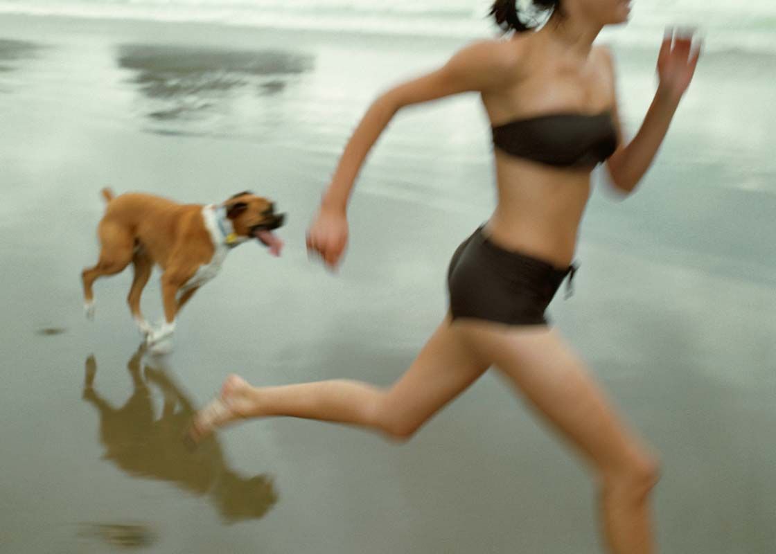 A woman and her dog running on the beach with motion blur