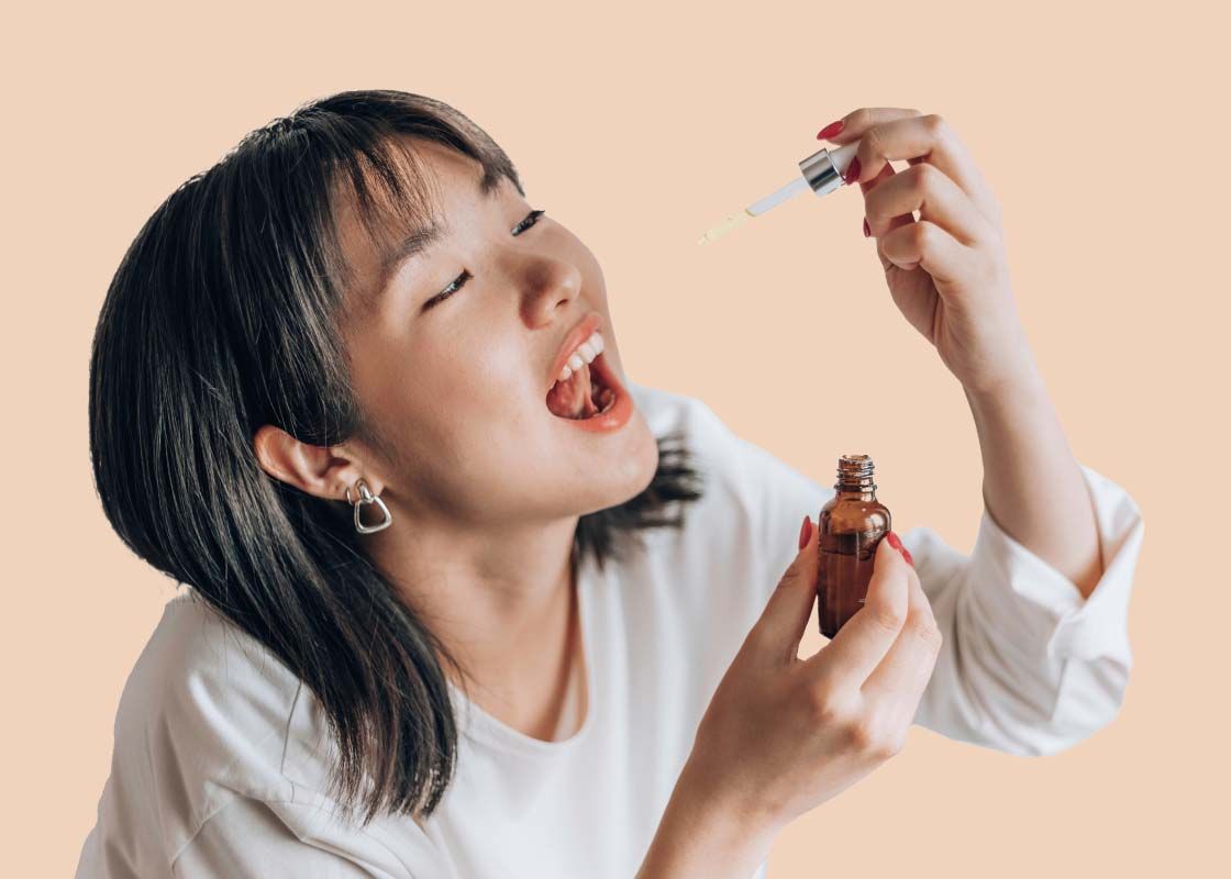 A woman's hand holding an amber dropper bottle in front of a cream background