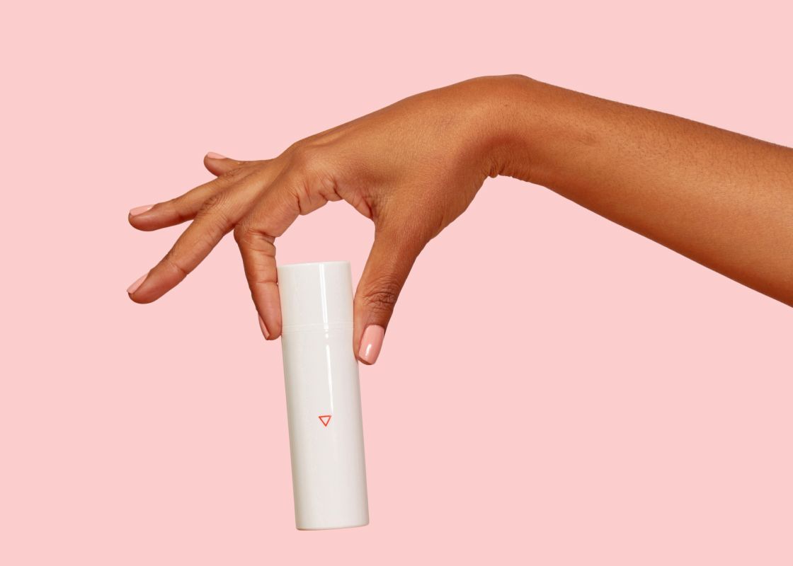 A woman's hand holding a Wisp menopause estriol cream bottle in front of a pink background