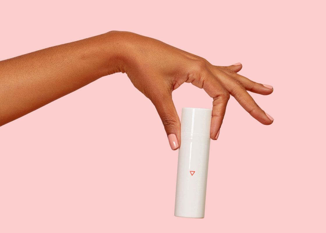 A woman's hand holding a Wisp menopause estriol cream bottle in front of a pink background