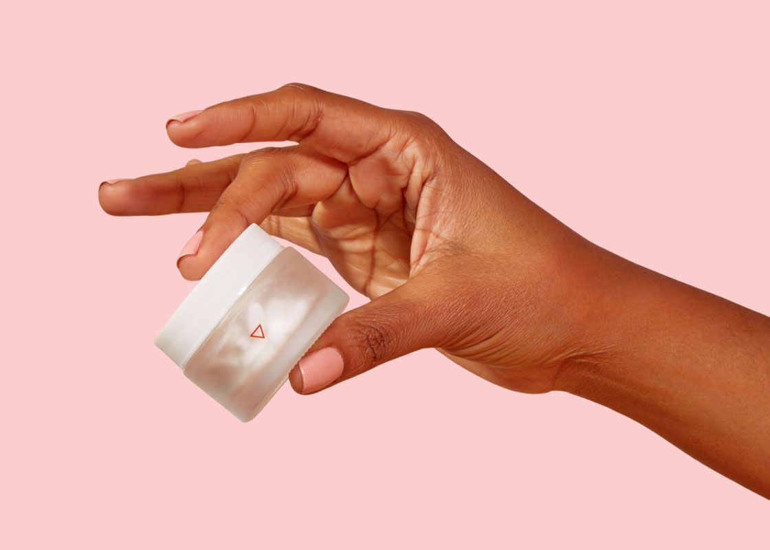 A woman's hand holding a small Wisp glass pill jar in front of a pink background