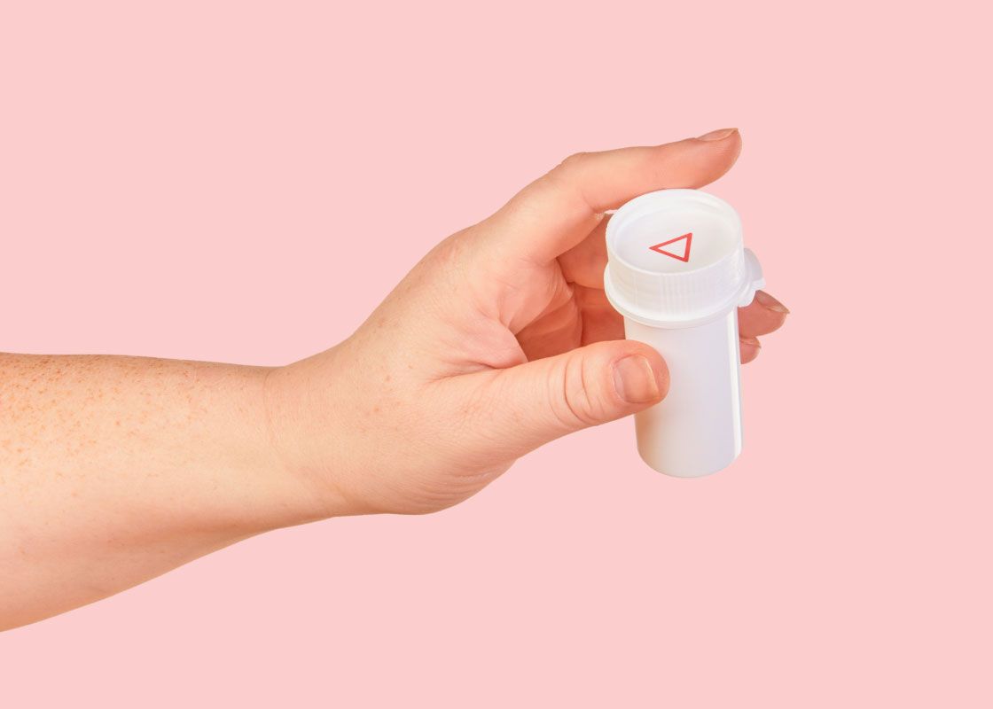 A woman's hand holding a Wisp pill vial of Spironolactone in front of a pink background