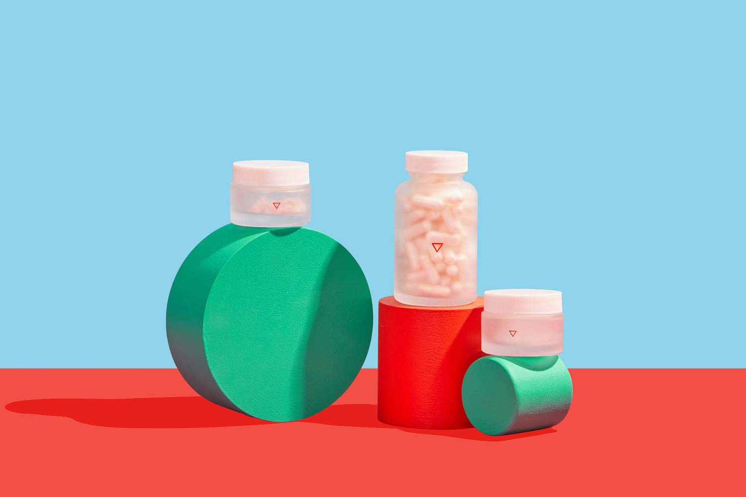 3 Wisp glass pill jars balanced on colorful abstract shapes with a light blue and red background