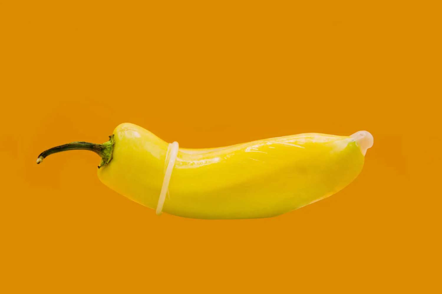 A yellow pepper with a condom on it in front of an orange background