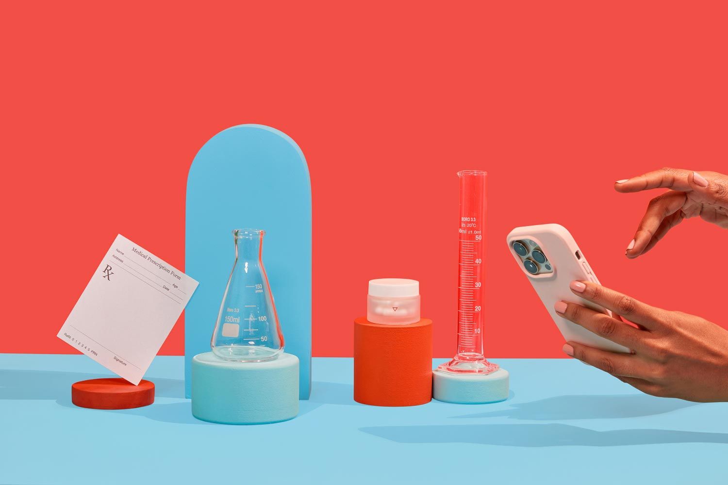 An RX script, testing tubes, and a small Wisp glass pill jar balanced on colorful abstract shapes with hands holding a mobile phone on a light blue surface with a red background