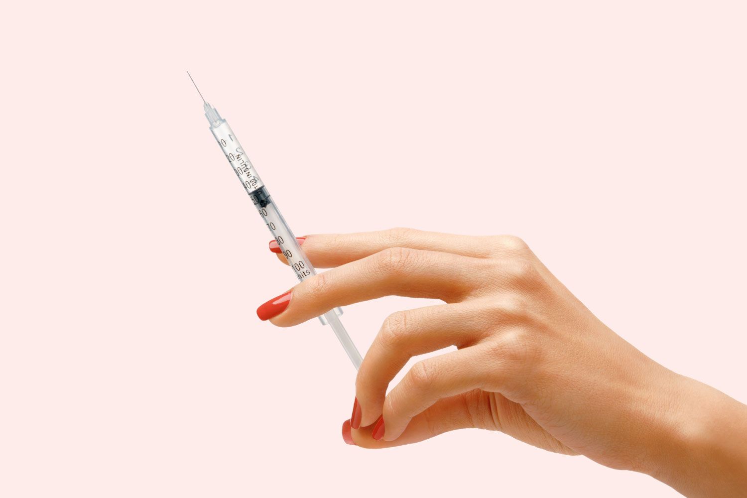 A woman's hand holding a syringe in front of a light pink background