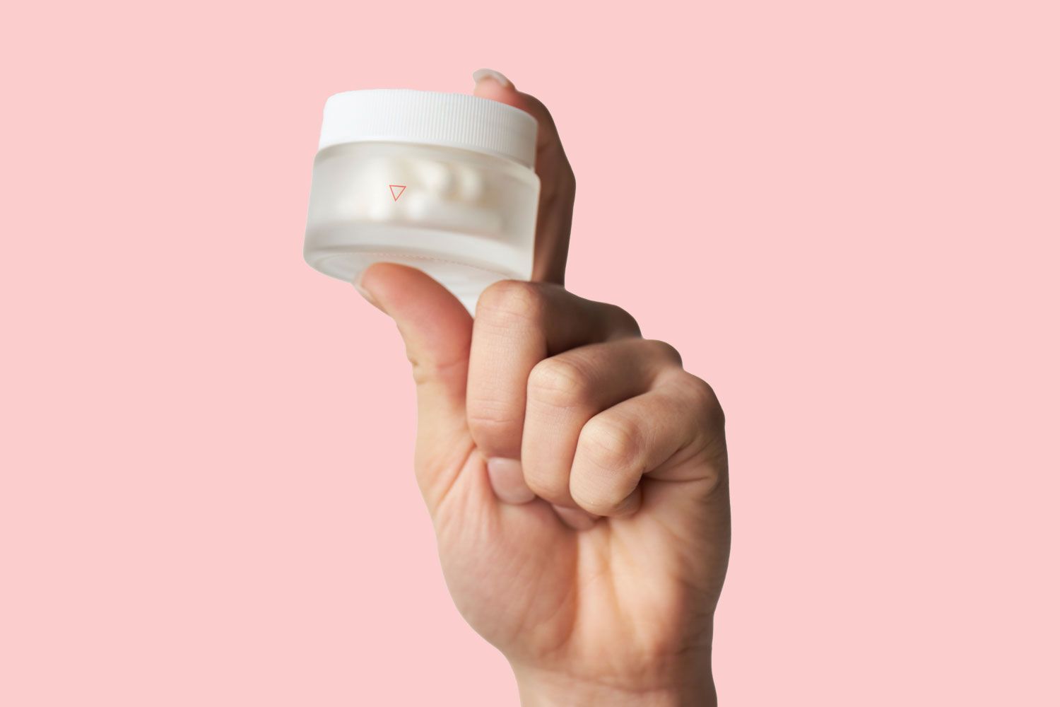 A woman's hand holding a Wisp glass pill jar with a pink background