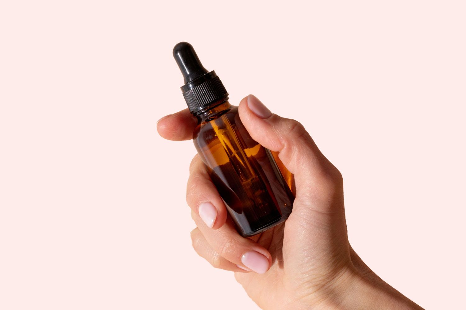 A hand holding an amber dropper bottle in front of a peach colored background