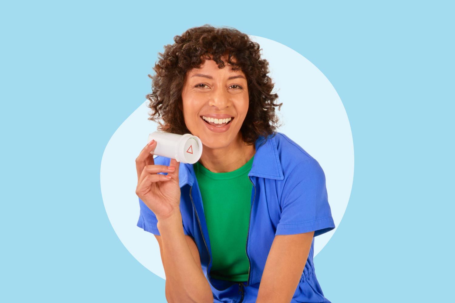 A woman wearing a green shirt and dark blue top is holding a bottle of spironolactone on a light blue background