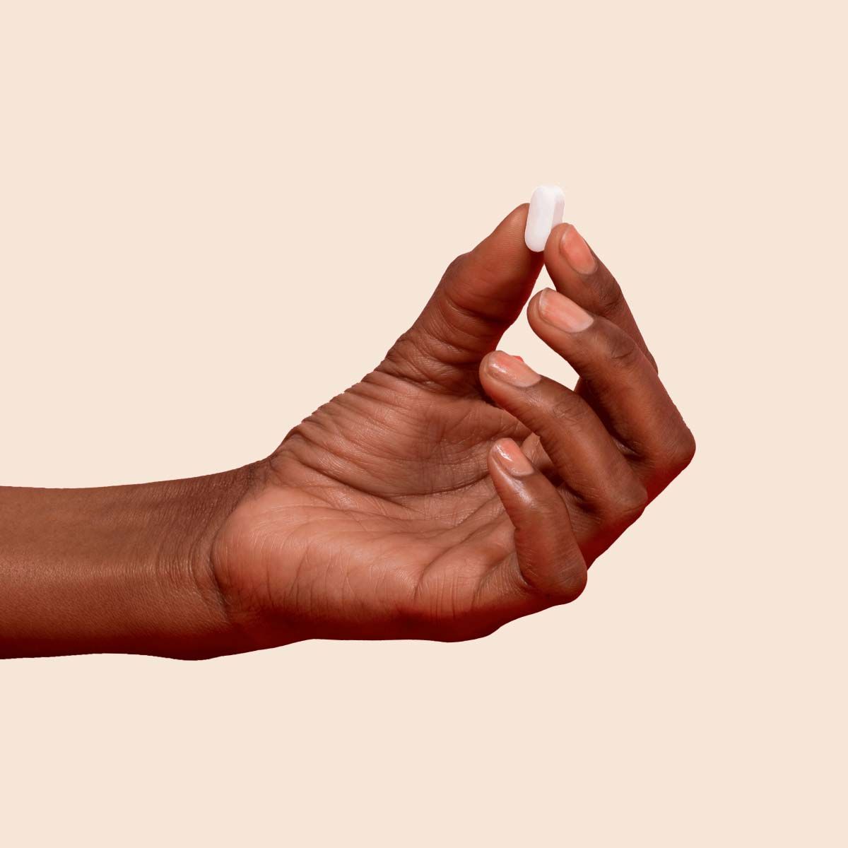 A person's hand holding a Metformin pill between their thumb and index finger with a cream background