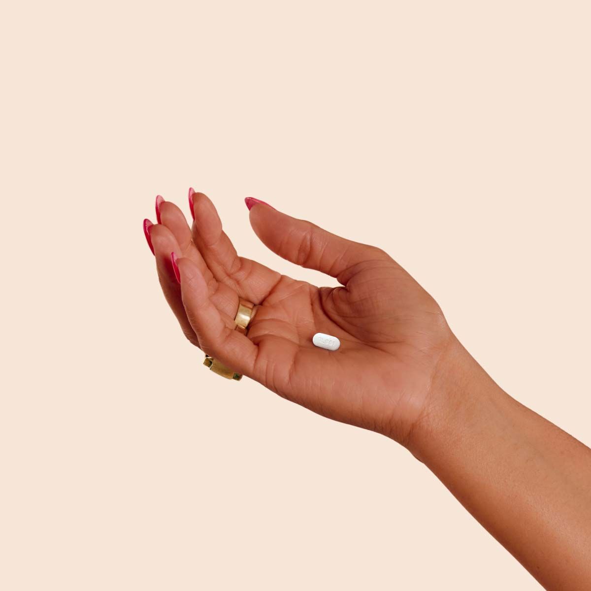 A person's hand holding a white pill with a cream background