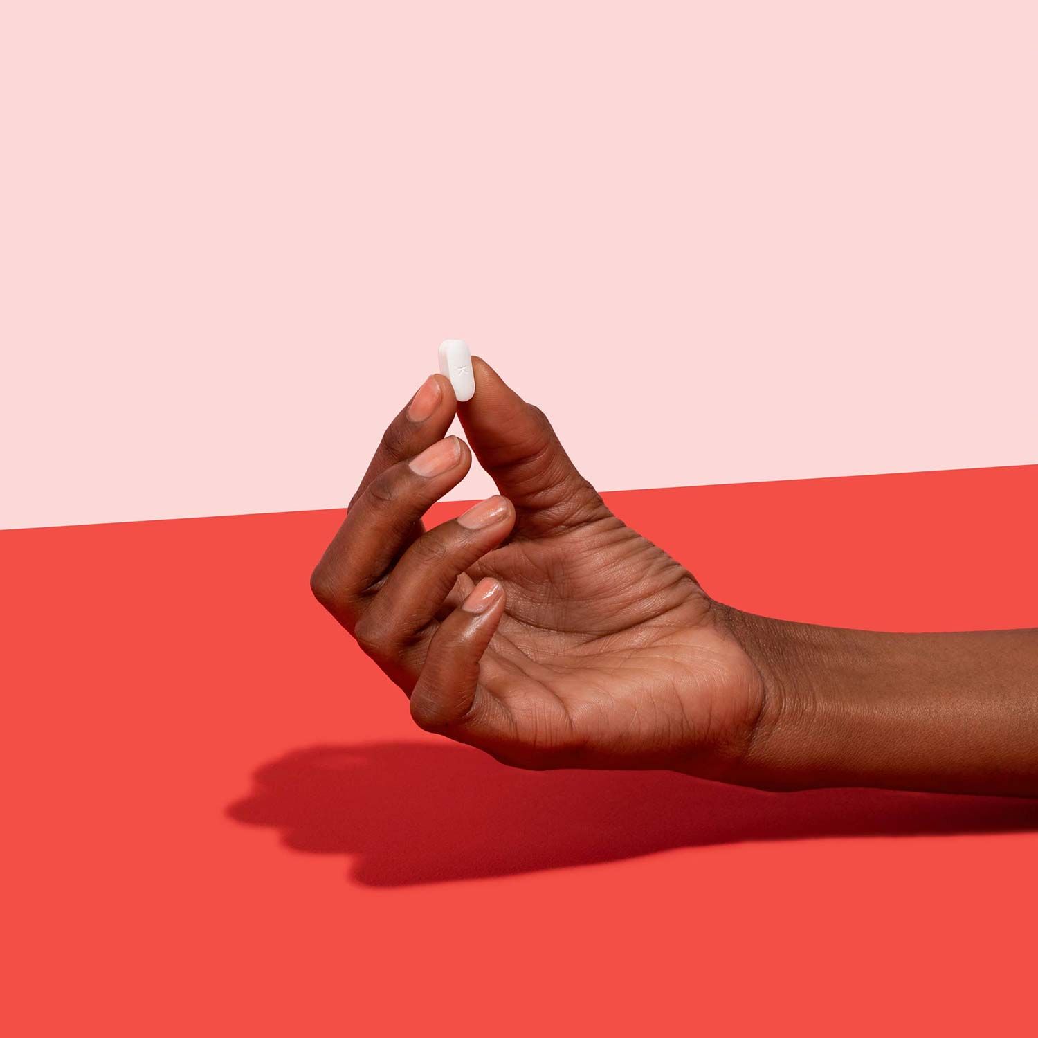 Hand holding BV antibiotic tablet to treat bacterial vaginosis on a pink background and red surface