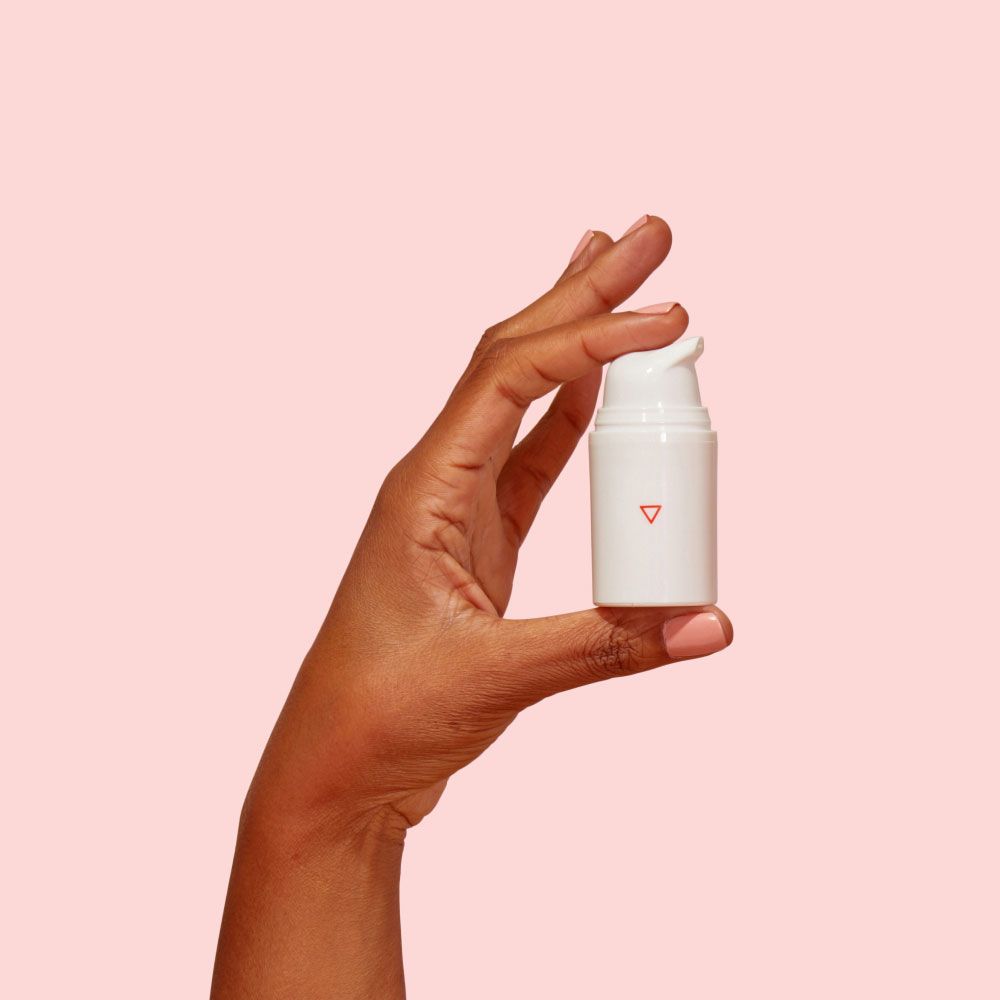 A woman's hand holding a Wisp pump bottle in front of a pink background