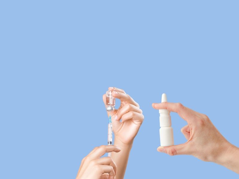light blue background with one hand holding a nasal spray and another pair of hands inserting a syringe into a vial