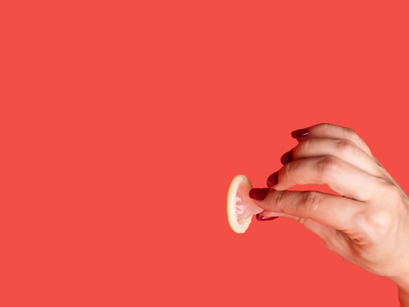 Person's hand holding a condom with a red background