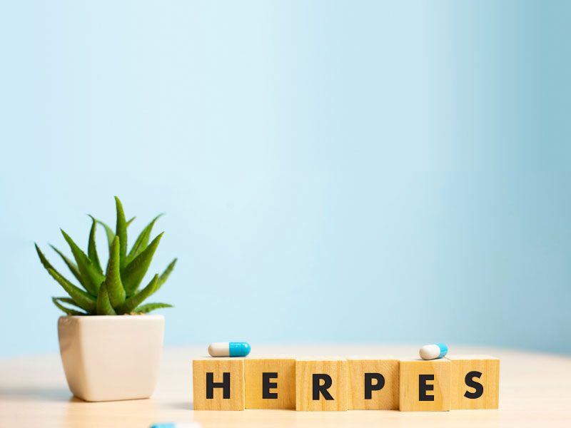 The word Herpes spelled out on wooden blocks with blue and white pills, a plant and a blue background