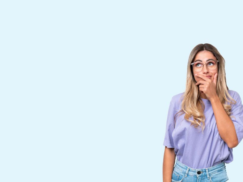 A woman with blonde hair wearing a purple shirt and jeans with a confused look on her face and a light blue background