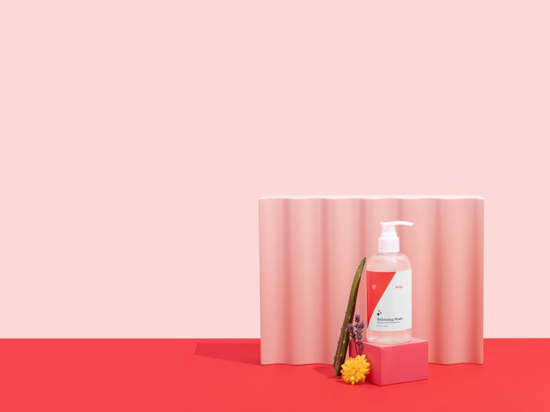 Wisp Balancing Wash with Aloe Vera, Lavender, Marigold and colorful abstract shapes on a pink and red background