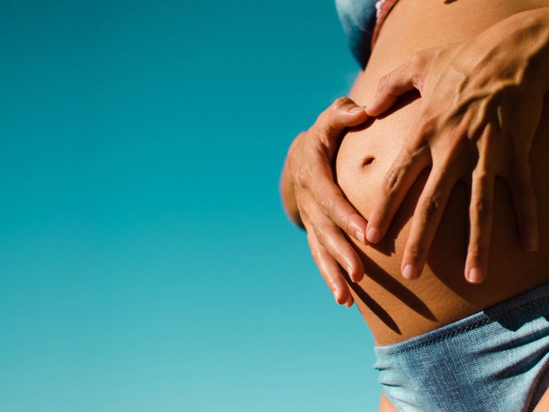 a pregnant woman in a blue bikini holding her stomach against a blue background