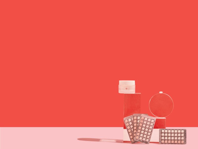 Birth control packets and a Wisp medication jar on a pink and red background