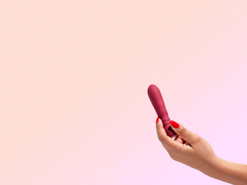 Hand holding a vibrator on a orange and lilac gradient background