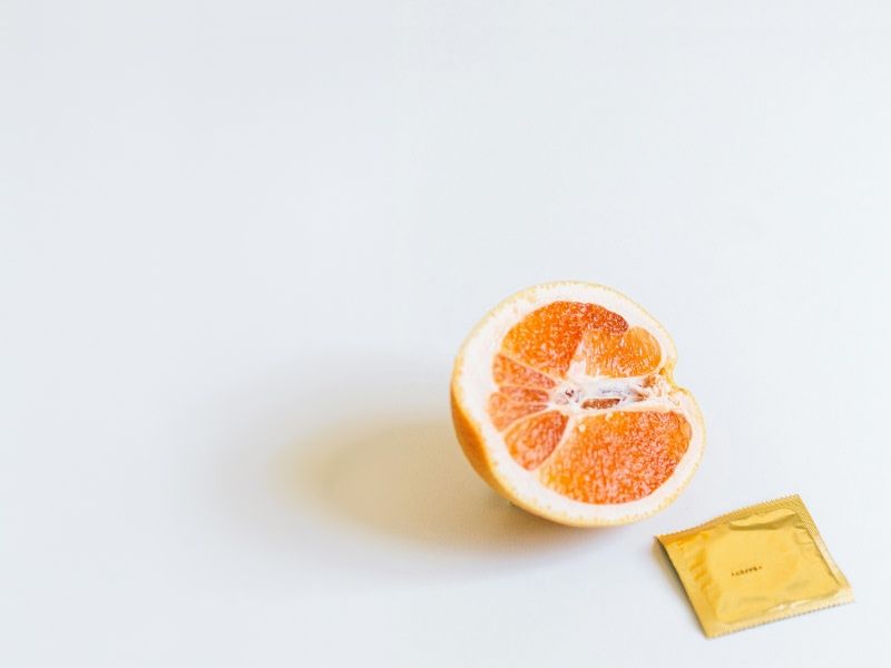 a white background with half an orange facing outwards next to a gold foil square packet