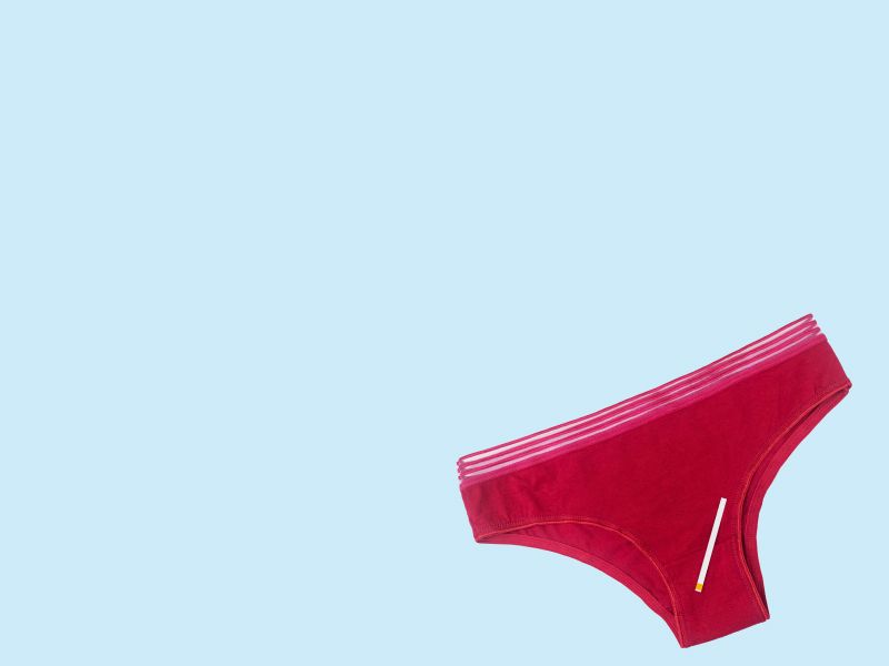 A pair of dark red women's underwear with a test strip laying on top on a blue surface