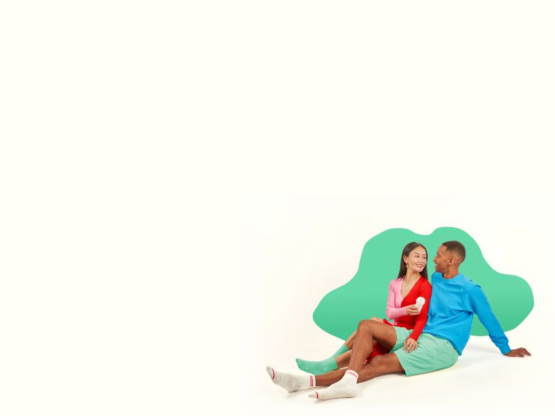 A woman and man smiling at each other while holding a Wisp pill vial on a pale yellow surface