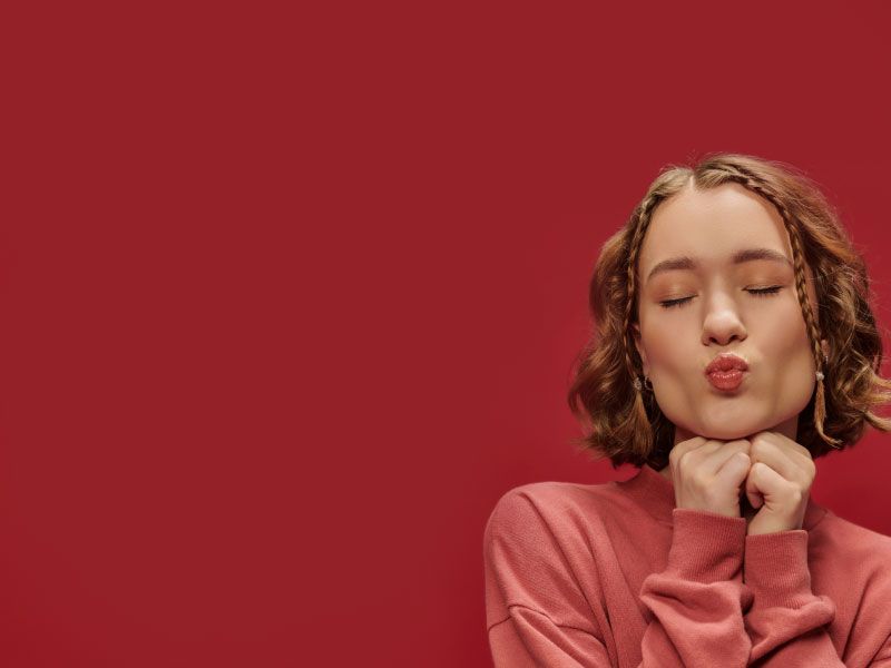 Woman wearing a pink sweater pucker her lips with a dark red background