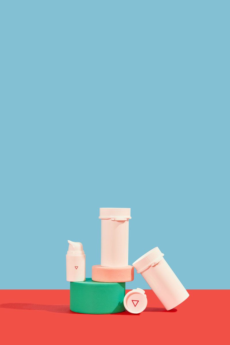 Wisp plastic pill vials and a pump bottle balanced on colorful abstract shapes on a red surface with a light blue background