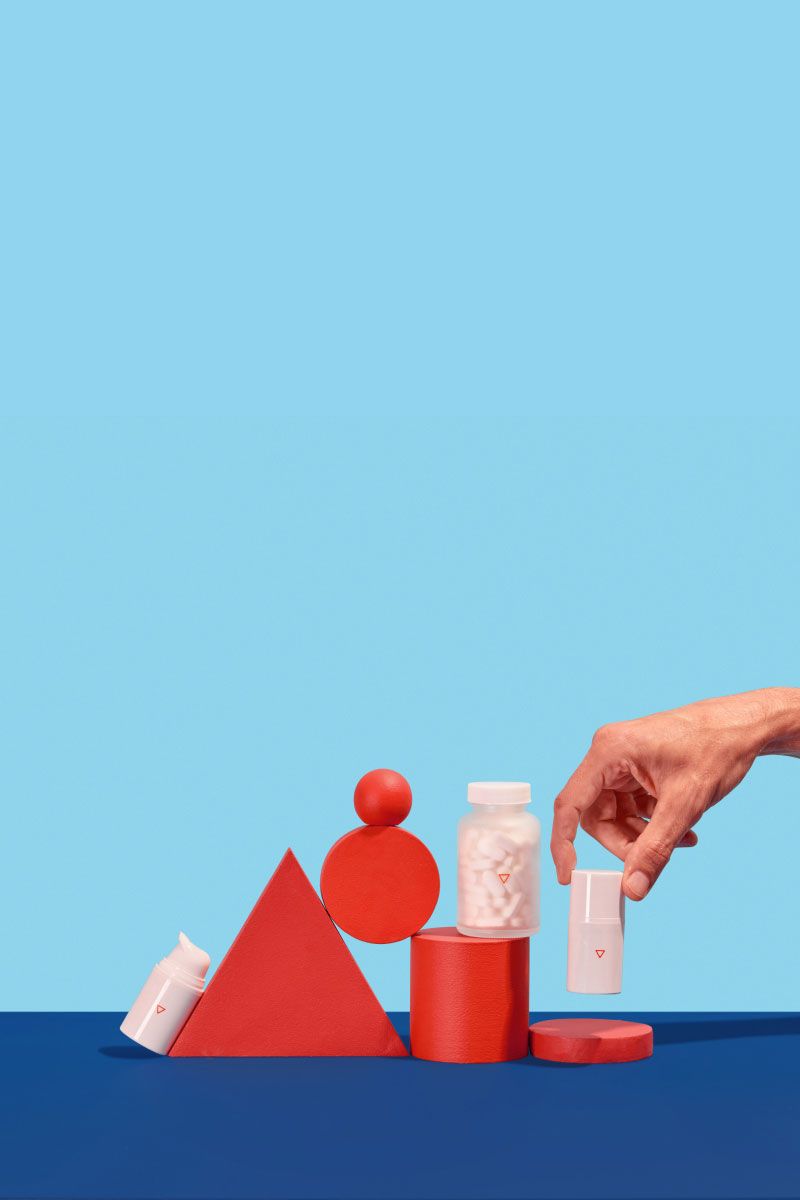 A man's hand picking up cold sore medication from a colorful geometric background