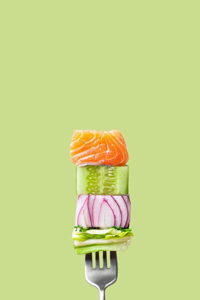 a fork spearing raw salmon and veggies against a green background