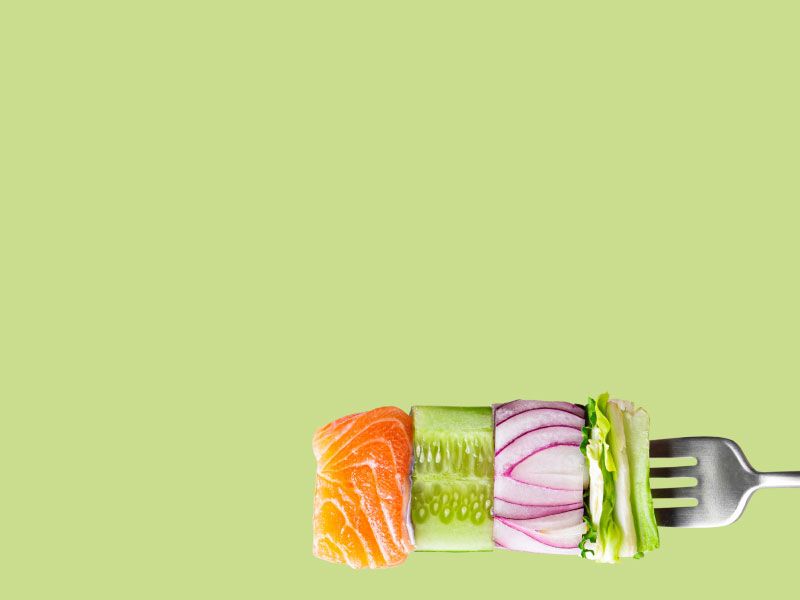 a fork spearing raw salmon and veggies against a green background